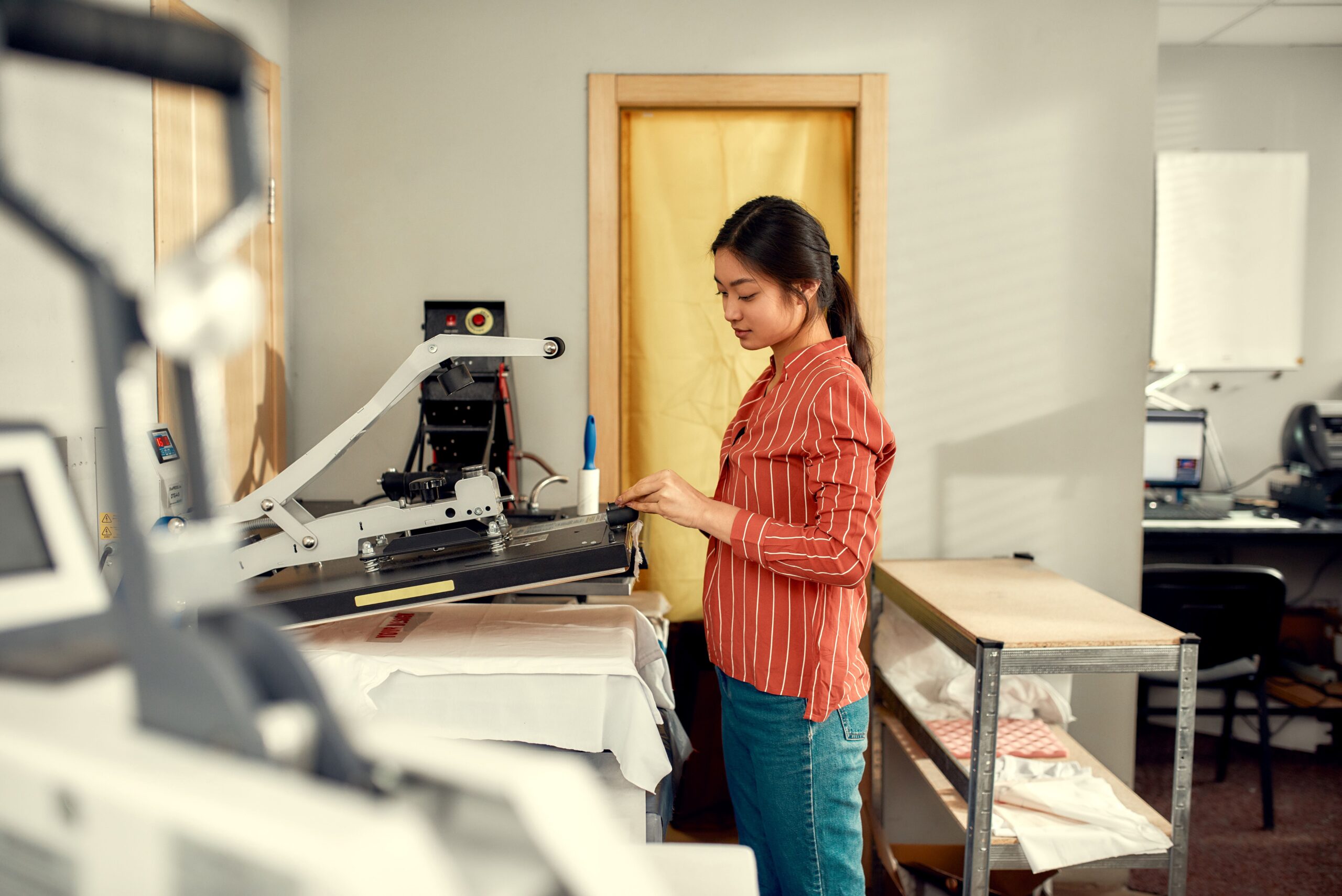 Woman using a heat press machine to apply a direct to film transfer to a shirt. 